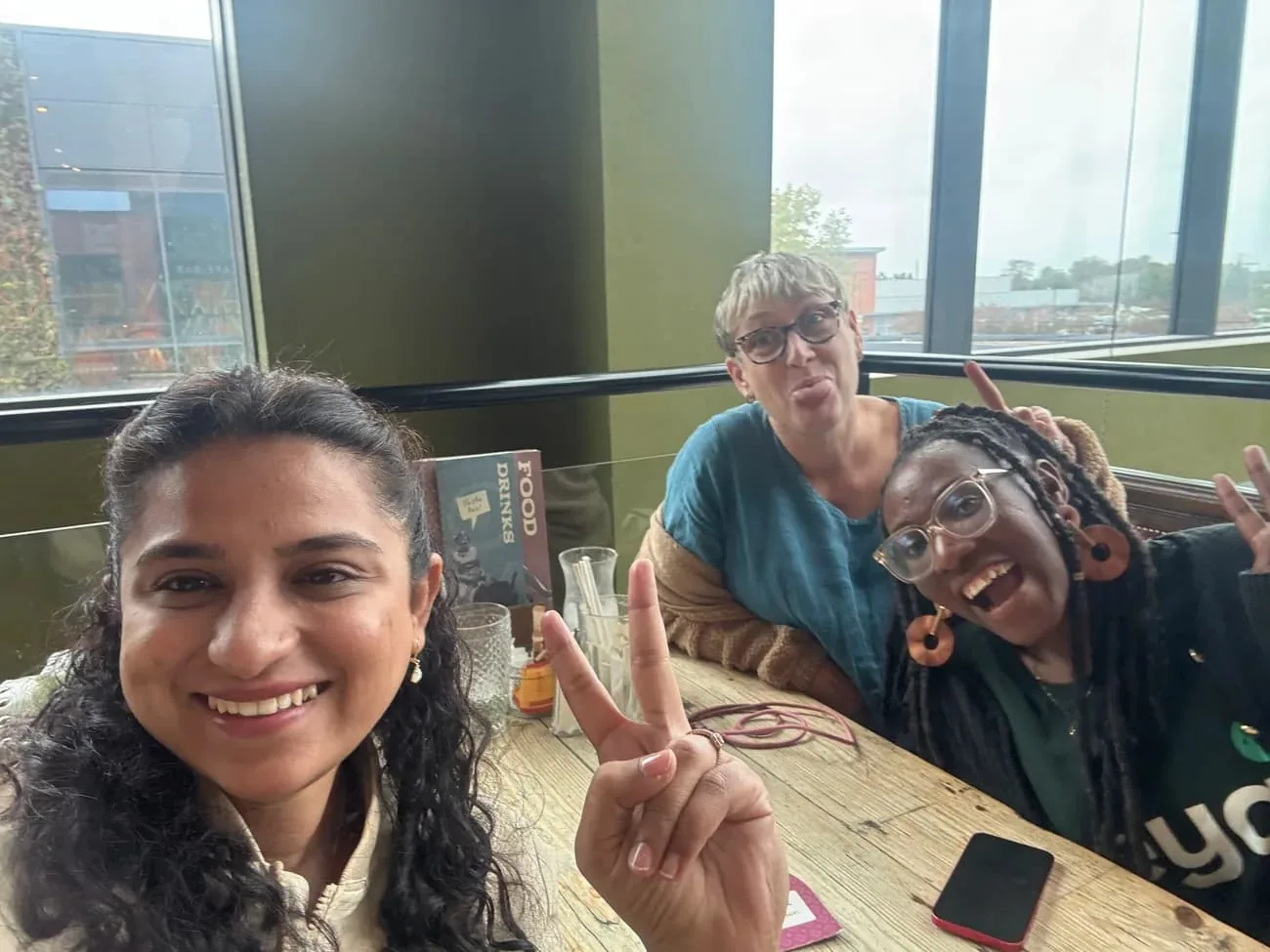 Three people smiling together around a pub table